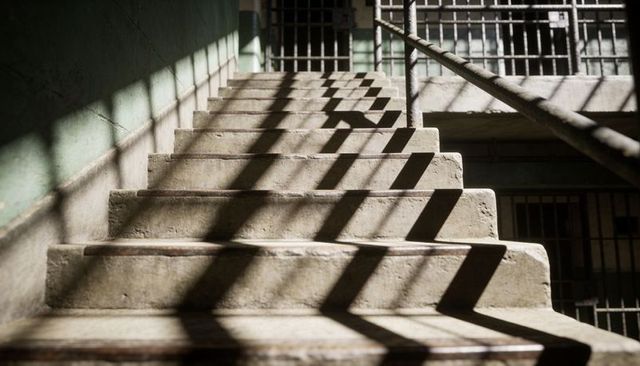 Worn concrete staircase casting grated shadow patterns over rusted handrail in abandoned prison