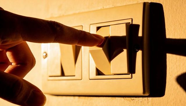 Pressing finger activating beige rocker light switch casting dramatic warm shadow