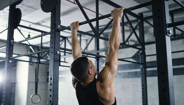 Muscular man doing pull-ups on industrial steel rig, sweaty strength training in warehouse gym