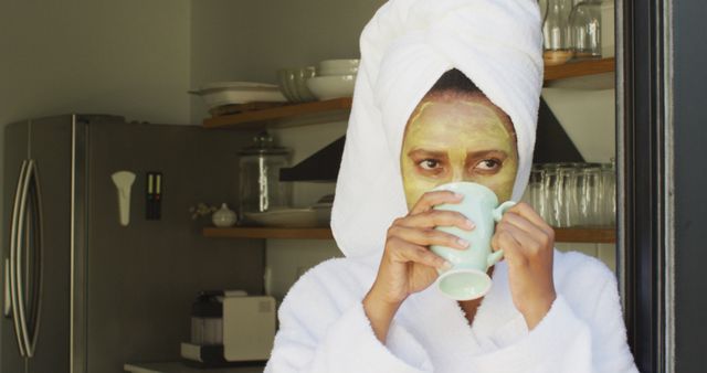 Happy african american woman with beauty mask on face, drinking coffee in kitchen - Download Free Stock Photos Pikwizard.com