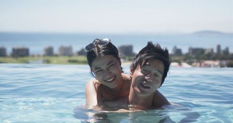 Asian couple embracing and smiling in rooftop infinity pool with coastline skyline view
