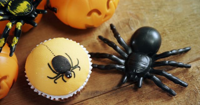 A Halloween-themed cupcake decorated with a spider sits next to plastic spiders and pumpkin containers, with copy space. These festive decorations create a playful and spooky atmosphere for a Halloween celebration.