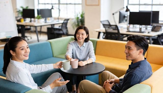 Asian colleagues sharing coffee and chatting in modern open plan office lounge