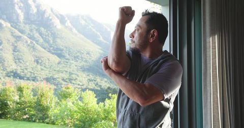 Mature asian man stretching arm near scenic window view