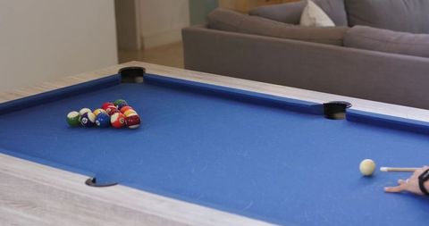 Mid adult male aiming cue on blue felt pool table in cozy living room casual billiards
