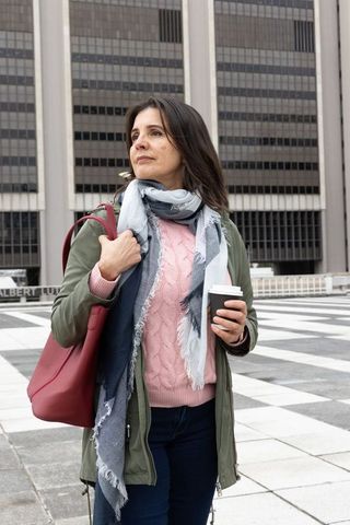 Middle-aged woman standing before office building holding coffee cup and red tote