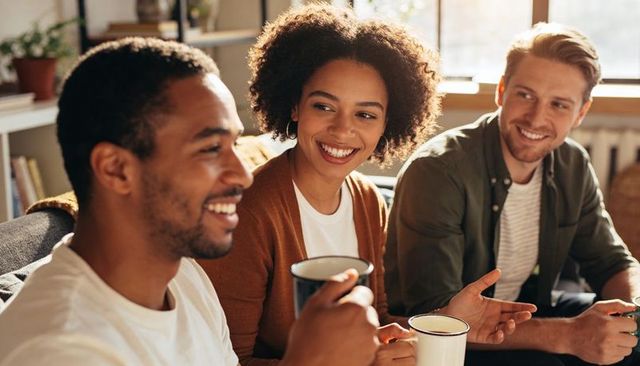 Friends chatting and sipping coffee on sunlit couch in cozy living room, warm conversation