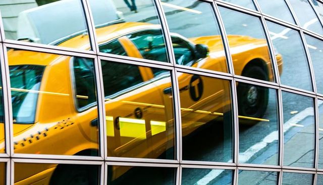 Reflecting yellow taxi stretching across curved glass facade showing door logo