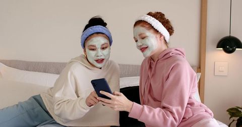 Sharing cozy at-home spa night wearing hoodies and facial masks while using phone