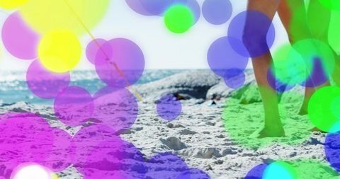 Sunlit beach walk with legs and feet in shorts, colorful bokeh overlays and sea horizon