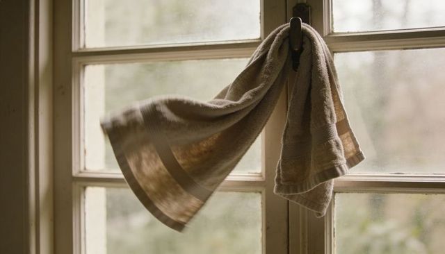 Beige terry towel billowing on window latch with soft morning light and smudged glass