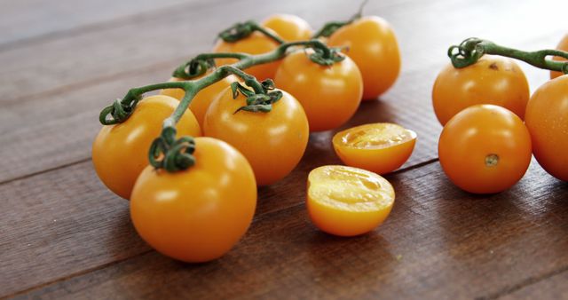 A cluster of ripe, yellow cherry tomatoes is arranged on a wooden surface, with one tomato cut in half to reveal the interior. Fresh and vibrant, these tomatoes are a staple in healthy salads and gourmet dishes.