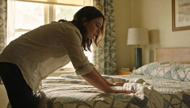 Smoothing quilt on sunlit bed, woman making bed in cozy bedroom morning routine