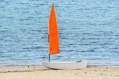 Small White Dinghy with Bright Orange Sail Resting on Sandy Shoreline with Calm Blue Sea