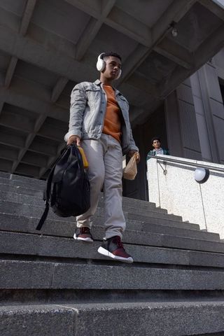 Young african american student descending campus stairs wearing denim jacket carrying backpack and h