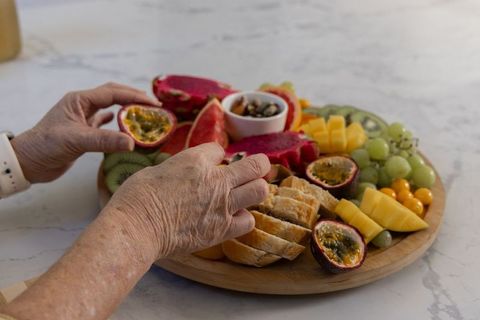 Senior hands arranging fruit platter on marble countertop with passion fruit and bread