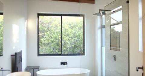 Sunlit minimalist bathroom featuring freestanding oval bathtub, black faucet, rain shower