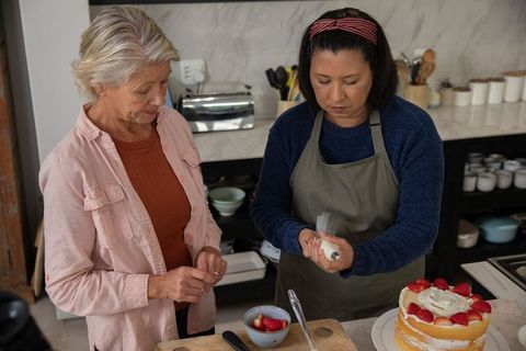 Two Women Decorating Layer Cake with Strawberries in Cozy Home Kitchen