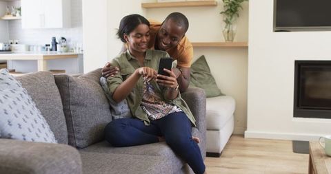 Happy Couple Relaxing on Sofa Enjoying Smartphone together