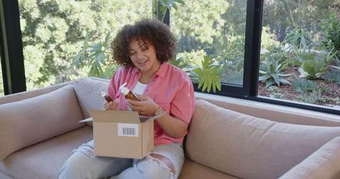 Woman examining skincare products on couch in bright living room