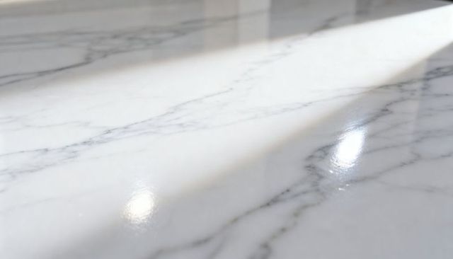 Polished white carrara marble countertop showing diagonal sunlight and glossy reflection