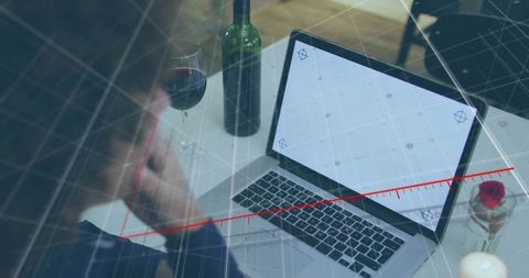 Man reflecting at laptop on elegant dining table with wine