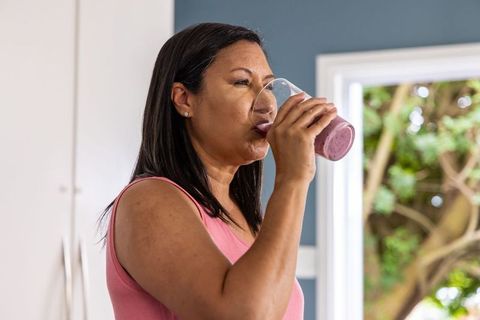Mature woman drinking pink smoothie by kitchen window for morning wellness routine