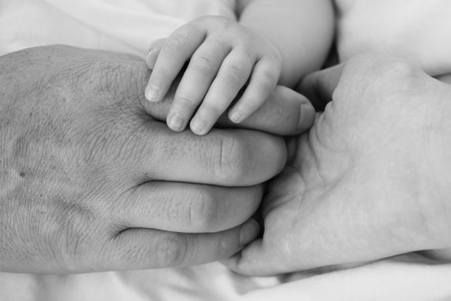 Close-up shot showing hands from three different generations in a black-and-white style, symbolizing connection, love, and family bonds. Ideal for use in articles or advertisements related to family, heritage, support systems, and generational relationships.