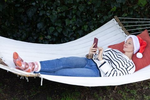 Relaxing in hammock wearing santa hat while scrolling smartphone