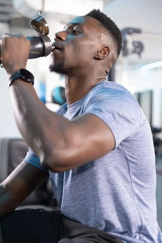 African american man drinking from metal shaker bottle at gym post-workout hydration and recovery