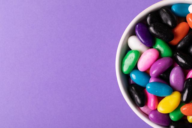 Bright and colorful candies in a white bowl placed on a purple background. Ideal for use in advertisements for candy brands, social media posts about sweets, or blog articles discussing unhealthy eating habits. The vibrant colors and ample copy space make it perfect for promotional materials and graphic design projects.