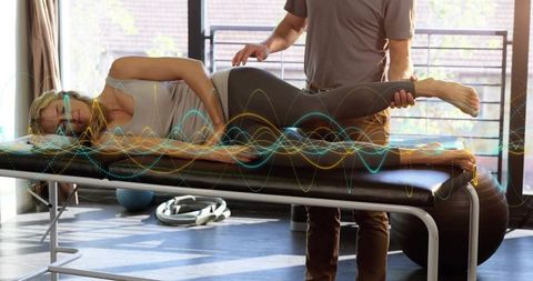 Clinician guiding side-lying patient through hip mobility exercise with biofeedback waveforms