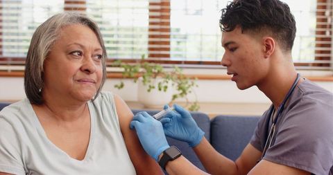 Young male nurse administering vaccine to senior woman