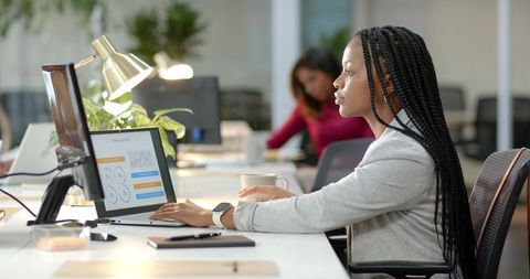 Young professional woman working at laptop with data charts in modern coworking office