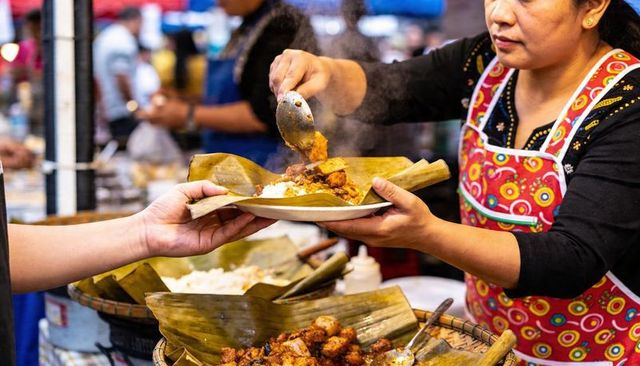 Scooping and serving steaming curry on banana-leaf plate at bustling night market stall