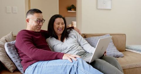 Senior Couple Laughing Together on Sofa with Laptop