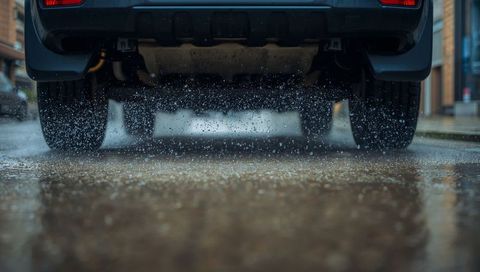 Low-angle dark suv rear tires spraying water across wet urban street with puddle splashes
