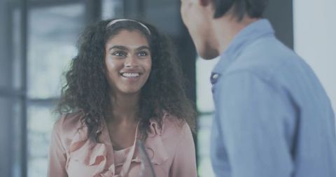 Smiling woman wearing pink ruffled blouse speaking with colleague in modern office meeting