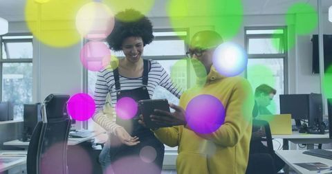 Young professionals collaborating on tablet in vibrant open-plan office with colorful bokeh