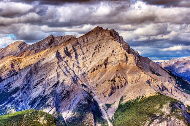 This image captures a stunning rocky mountain peak with a dramatic cloudy sky overhead. It is ideal for travel brochures, adventure blogs, and nature-related websites. Its strong visual impact makes it suitable for wall art, posters, and calendar images.