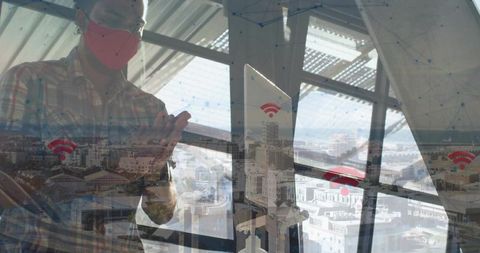Masked man standing by office window with wi-fi network overlay over urban skyline