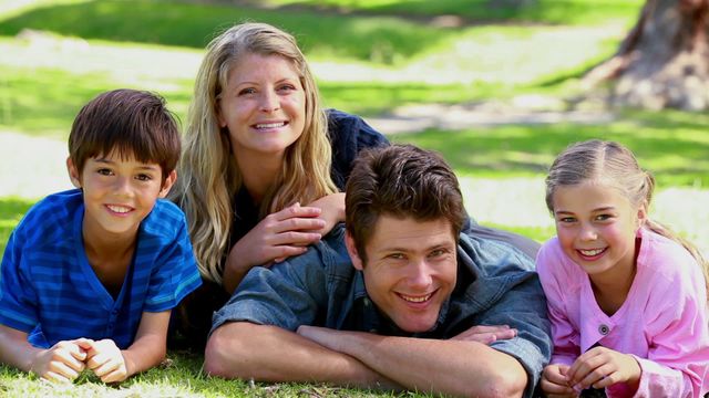 Happy family lying on grass. It shows two parents with two children enjoying a sunny day in park. Ideal for concepts of family bonding, outdoor activities, happiness, and lifestyle promotions.