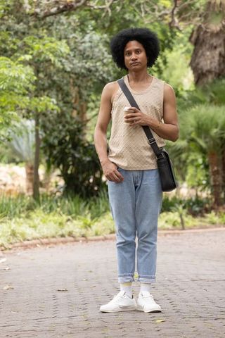 African american man standing in park holding coffee wearing casual tank and crossbody bag