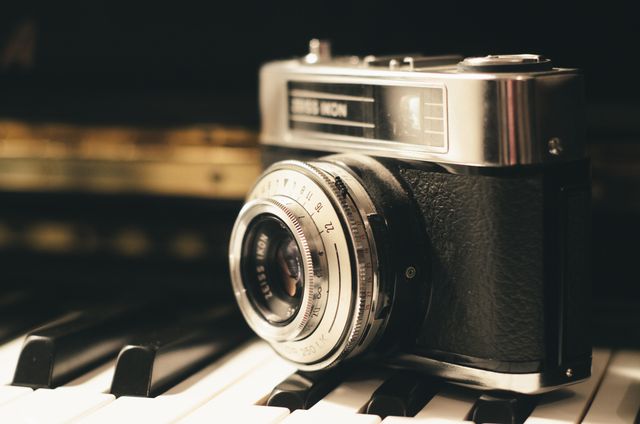 Vintage camera placed on piano keyboard, showcasing classic and elegant aesthetics. Ideal for concepts relating to photography, music, retro style, and vintage themes. Perfect for use in blogs, advertisements, and design projects emphasizing nostalgia and timeless artistry.