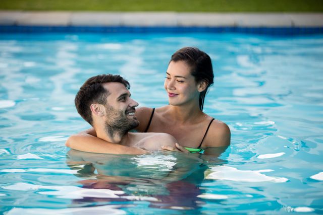 Young romantic couple embracing in a swimming pool, enjoying a summer day. Perfect for use in advertisements for vacation resorts, travel brochures, romantic getaways, and lifestyle blogs focusing on relationships and leisure activities.