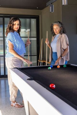Multiracial women playing pool in modern lounge, social leisure and friendship moment