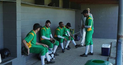 Multiracial baseball team resting in dugout with coach preparing for game strategy