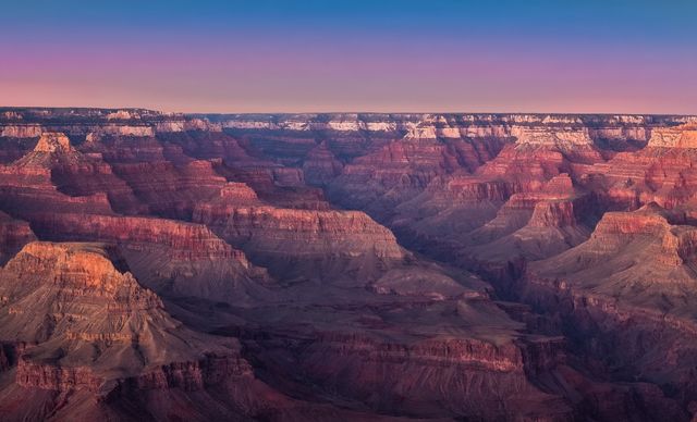 Image depicts a breathtaking sunset over the Grand Canyon National Park showcasing the vibrant, colorful rock formations illuminated by the twilight. Ideal for use in travel blogs, nature magazines, educational content about national parks, or tourism promotional materials.