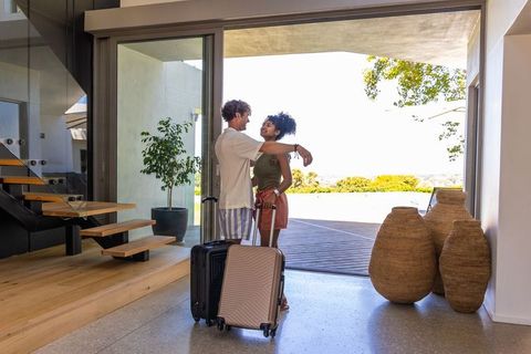 Couple embracing at modern home entry with luggage and sunlit terrace view