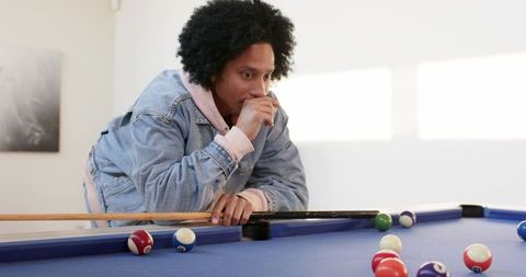 African american man concentrating on billiards shot leaning over blue pool table indoors
